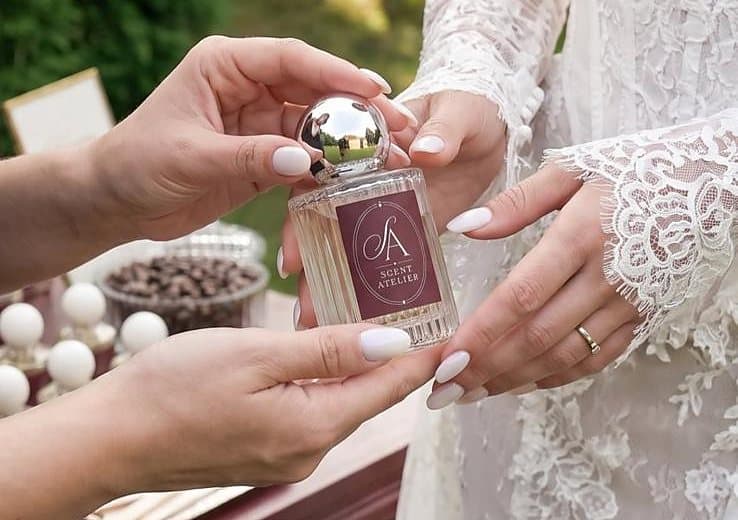 Mladenka u čipkastoj haljini prima bočicu parfema od 30 ml sa srebrnim čepom i oxblood etiketom.